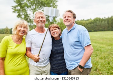 Group of seniors as friends take a selfie with smartphone on selfie stick - Shutterstock ID 1310845913