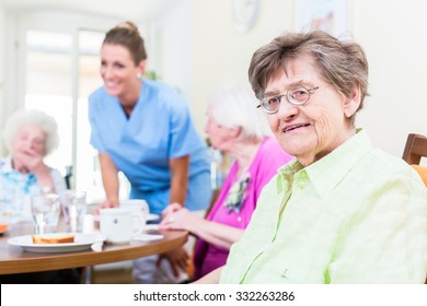 Group Of Seniors Having Food In Nursing Home, A Nurse Is Serving