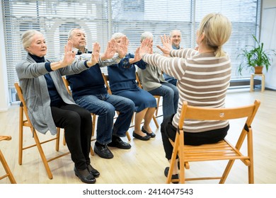 Group of seniors practicing chair gymnastics with instructor in retirement home - Powered by Shutterstock