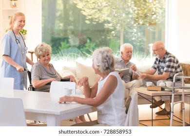 Group Of Seniors Spending Free Time In Bright Living Room With Big Window At Nursing House