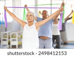 Group of seniors using resistance bands to stretch their arms and body while kneeling on mats