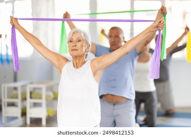 Group of seniors using resistance bands to stretch their arms and body while kneeling on mats - Powered by Shutterstock