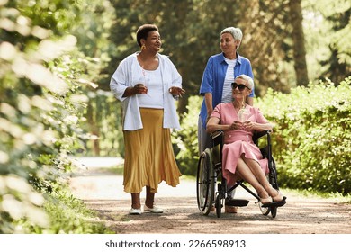 Group of seniors with woman in wheelchair enjoying walk in park together - Powered by Shutterstock