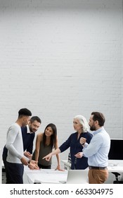 Group Of Serious Business People In Smart Casual Wear Having A Brainstorm Meeting While Standing At The Office