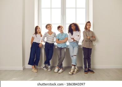 Group Of Serious Diverse Kids Looking At Camera Standing By Window With Arms Folded In Hall At School Or Educational Center. Success, Confidence In Future, Conflict Resolution In Children's Community