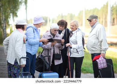 A Group Of Serious Senior Friends With Suitcases Using Tablet And Waiting For A Train On The Platform