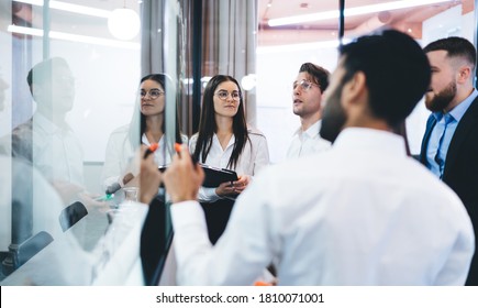 Group of serious successful business partners in formal wear standing in modern office and communicating about startup ideas while having meeting