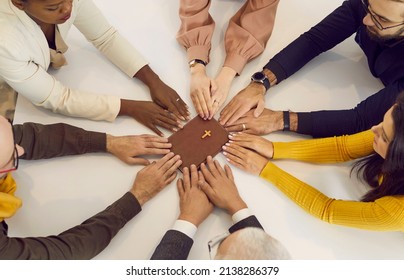 Group of several different young and senior mixed race multiracial multiethnic people who belong to the Christian church holding hands on the Holy Bible and praying together during a religious meeting