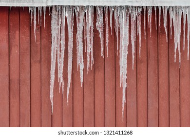 A group of sharp white and red transparent icicles is hanging down from the roof of a red building in winter
