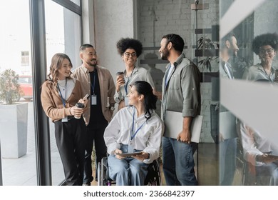 group shot of happy diverse team looking at each other in office, wheelchair user, inclusion
