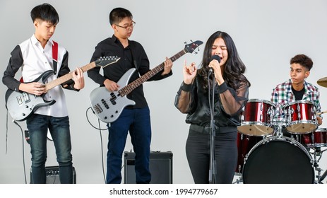 Group Shot Of Teenage Musicians Playing The Music And Singing Song. Young Students Play Bass Guitar, Electric Guitar, Drum, And Keyboard. Concept Of A School Music Band And Teenager Lifestyle