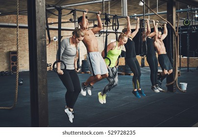 Group Of Six Attractive Young Male And Female Adults Doing Pull Ups On Bar In Cross Fit Training Gym With Brick Walls And Black Mats