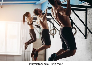 Group of six attractive young male and female adults doing pull ups on bar in cross fit training gym with brick walls and black mats - Powered by Shutterstock