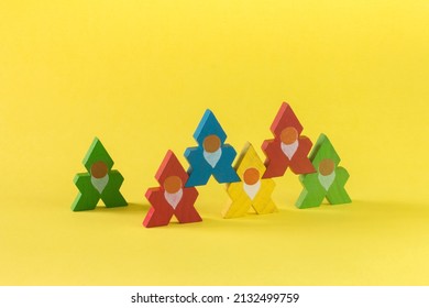 A group of six brightly colored, old-fashioned stacking wooden toy cut-out troll or elf figurines in a pyramid formation, on a yellow background. Concept of play, teamwork and cooperation.