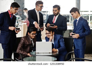 Group of six indian business man in suits sitting at office on cafe looking at laptop and drinking coffee.