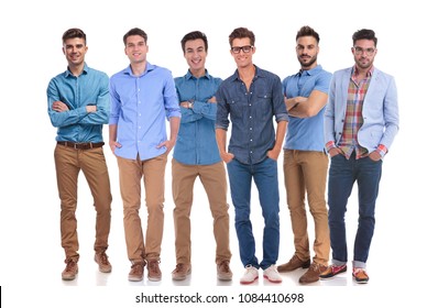 Group Of Six Young Casual Men Standing Confidently On White Background And Smiling. Three Of Them Are Standing With Their Arms Crossed And The Other Three With Hands In Pockets