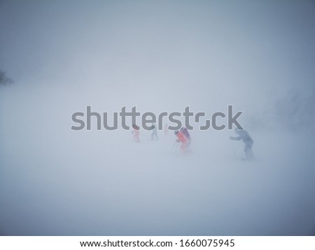 Group of skiers under the strong wind condition on the mountain while skiing. The vision is blurry and not clear because of snow