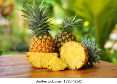 Group of sliced and half of pineapple(Ananas comosus) on wooden table with blurred garden background.Sweet,sour and juicy taste.Have a lot of fiber,vitamins C and minerals.Fruits or healthcare concept