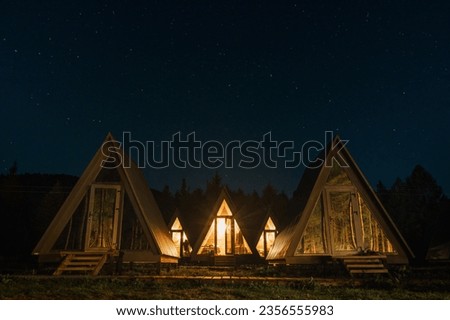 A group of small houses in a campsite. The houses glow in the starry night. Rest in the mountains.