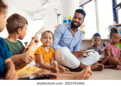 Group Of Small Nursery School Children With Man Teacher Sitting On Floor Indoors In Classroom, Playing.