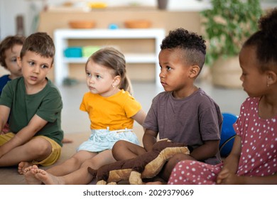 Group of small nursery school children sitting on floor indoors in classroom, listening to teacher. - Shutterstock ID 2029379069