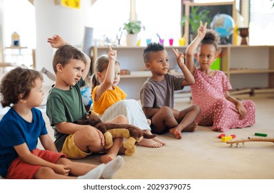 Group of small nursery school children sitting on floor indoors in classroom, raising hands. - Shutterstock ID 2029379075
