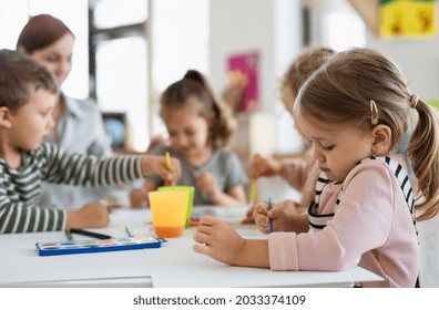 Group of small nursery school children with teacher indoors in classroom, painting. - Shutterstock ID 2033374109