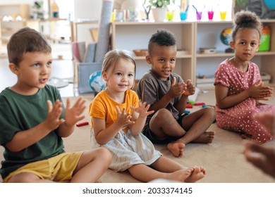 Group of small nursery school children sitting on floor indoors in classroom, clapping.