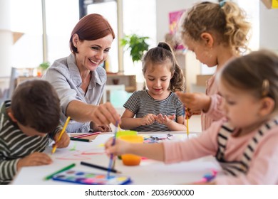 Group Of Small Nursery School Children With Teacher Indoors In Classroom, Painting.