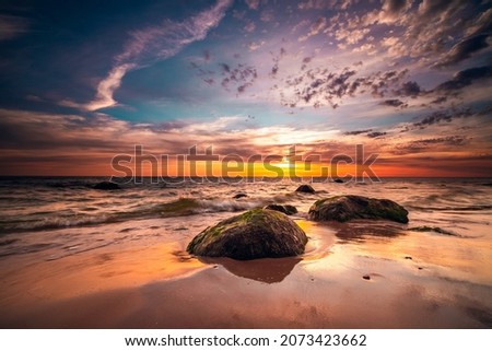 A group of small rock formations and a dramatic sunset sky over the tranquil Baltic Sea in Lithuania