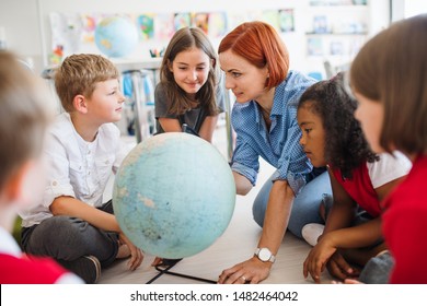 A Group Of Small School Kids With Teacher Sitting On The Floor In Class, Learning.