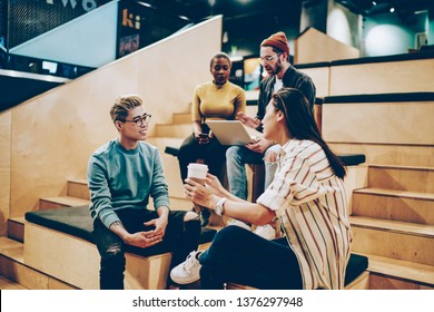 Group of smart multiracial teen students spending time together planning project in campus, trendy dressed male and female hipster guys communicating in coworking space during free time on break