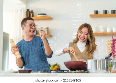 Group Of Smiling Asian People Friends Enjoy Cooking With Talking Together In The Kitchen At Home. Happy Man And Woman Having Dinner Party Meeting Celebration Eating Food Together On Holiday Vacation