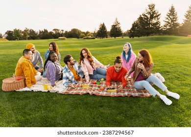 Group smiling attractive multiracial friends wearing colorful clothing relaxing, sitting on blanket in park, talking, laughing, eating food.  Diversity, friendship, picnic concept	 - Powered by Shutterstock