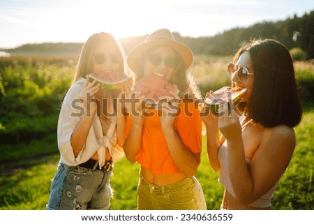 Group of smiling best friends have fun and eat watermelon on a hot summer day at a picnic. Three friends are relaxing and enjoying nature. The concept of vacation, picnic, friendship.