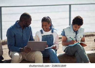 Group Of Smiling Black Kids With Teacher Using Laptop Together During Outdoor Lesson In Summer School