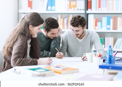 Group of smiling college students studying together at the library and working on a project