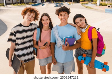 Group of smiling diversity teenagers high school pupils friends classmates college students boys and girls with bags meeting in skate park sport court outside riding in skateboard looking at camera - Powered by Shutterstock