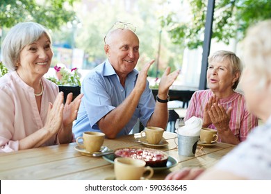 Group of smiling elderly people gathered together in outdoor cafe for tea-drinking and applauding joyfully - Powered by Shutterstock