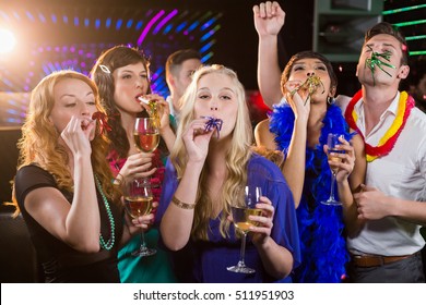 Group Of Smiling Friends Blowing Party Horn While Having Glass Of Champagne In Bar