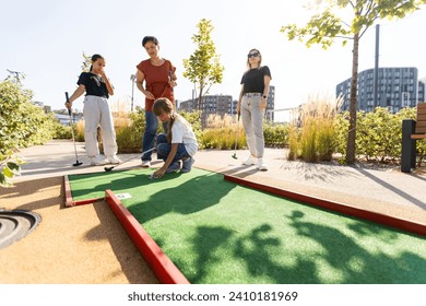 Group of smiling friends enjoying together playing mini golf in the city. - Powered by Shutterstock