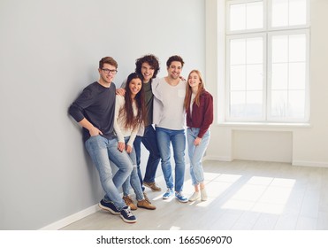 Eine Gruppe lächelnder Freunde steht in einem hellen Raum mit Fenster.