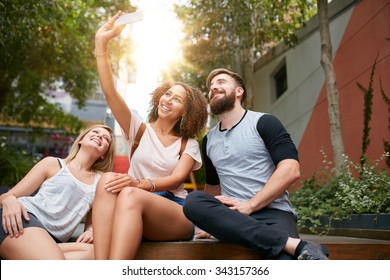 Group Of Smiling Friends Taking Selfie With Smart Phone. Multiracial Man And Women Enjoying Themselves Outdoors And Taking Pictures With Mobile Phone.