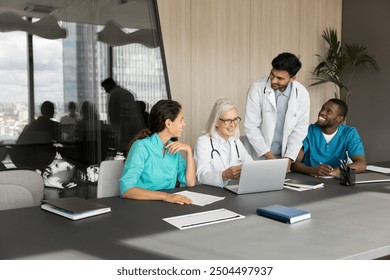 Group of smiling general practitioners gathered together in modern conference room for researching or teamwork, using laptop, laugh, enjoy friendly successful workflow, discussing work-related issues - Powered by Shutterstock