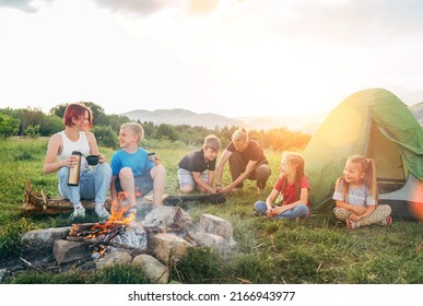 Group of smiling kids has a merry conversation near a smoky campfire. They drinking tea from a thermos, two brothers set up the green tent. Happy family outdoor picnic camping activities concept - Shutterstock ID 2166943977