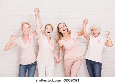 Group of smiling ladies with pink ribbons cheering and holding hands - Shutterstock ID 680520391