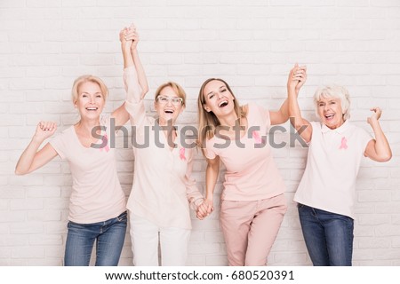 Group of smiling ladies with pink ribbons cheering and holding hands