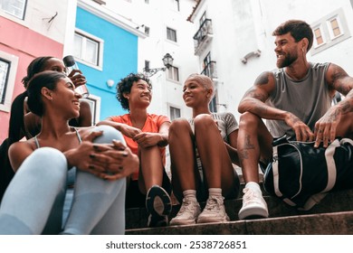 Group of smiling male and female athletes resting and chatting on urban steps after a workout, enjoying camaraderie and hydration - Powered by Shutterstock