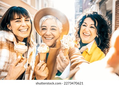 Group of smiling mature women eating ice cream cone outside in a sunny day - Three older friends girls take a happy selfie while walking at city - Concept about elderly people, food and joyful weekend - Powered by Shutterstock