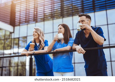 A group of smiling medical professionals in scrubs enjoying a coffee break outside, capturing teamwork, relaxation, and camaraderie in a modern healthcare setting. - Powered by Shutterstock